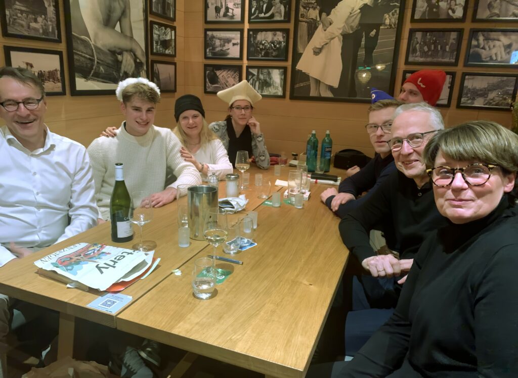 Andreas Franke, Justus Franke, Daniela Bristot, Anne Henter, Ansgar Rahmacher, Bodo Fink, Annette Franke sitzen an einem Restauranttisch und haben bunte Hüte auf.